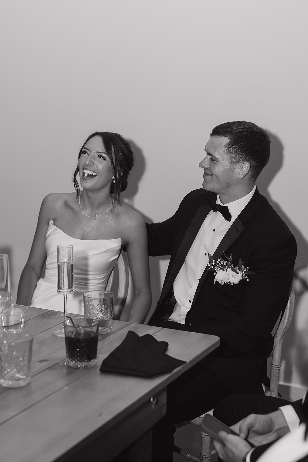 A black and white photo of the bride and groom laughing during their speeches during their wedding reception