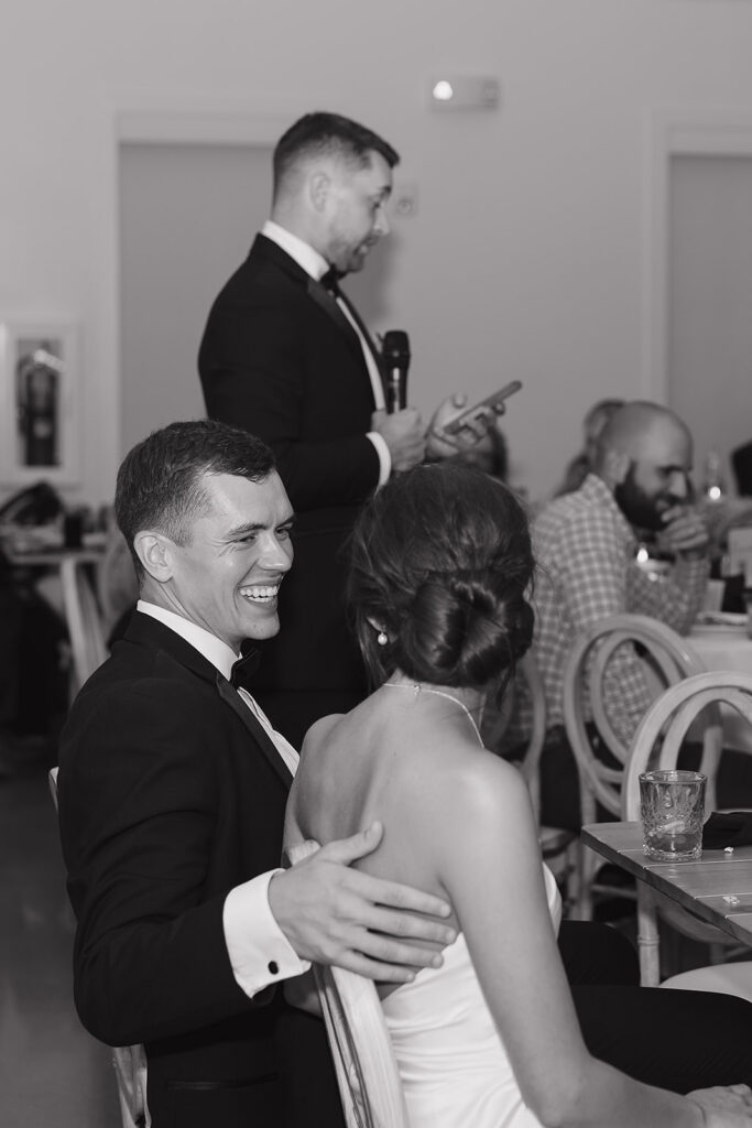 A black and white photo of the bride and groom laughing during their speeches during their wedding reception at Willow on Grand, a Des Moines Wedding Venue.