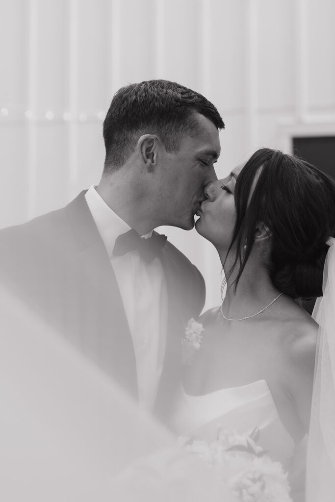 Close up black and white photo of the bride and groom kissing, framed softly through her veil for a timeless wedding portrait.