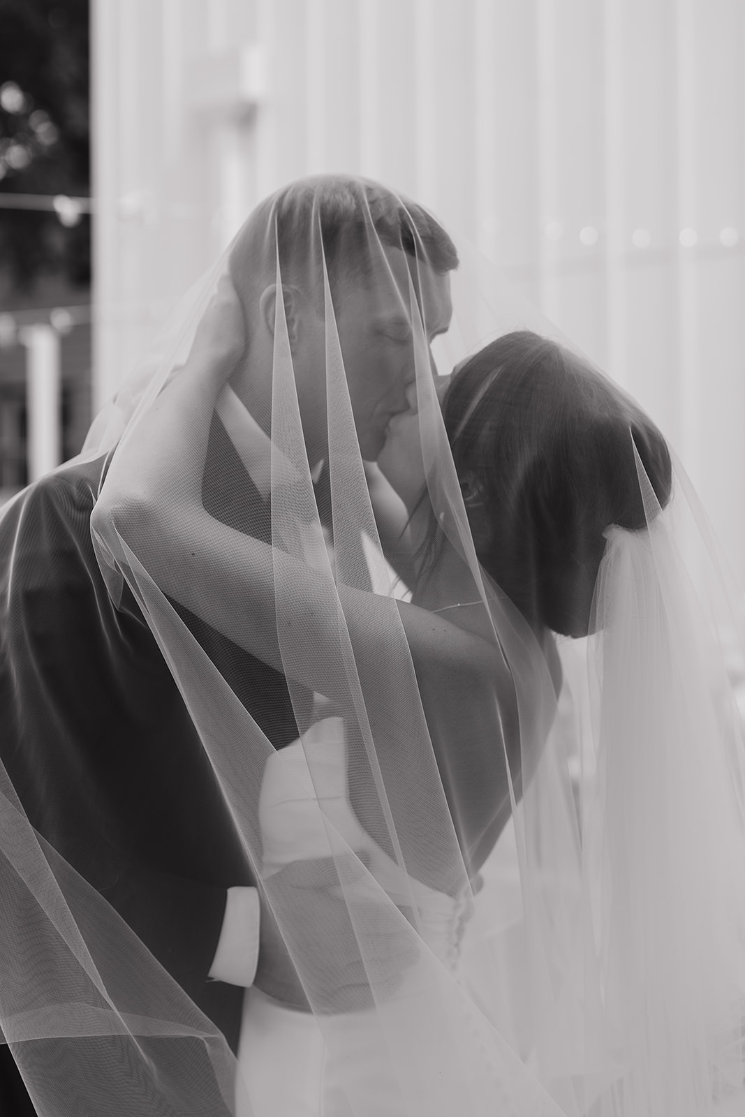 Romantic black and white portrait of the bride and groom kissing under her veil inside a Des Moines wedding venue, creating a soft and intimate silhouette.