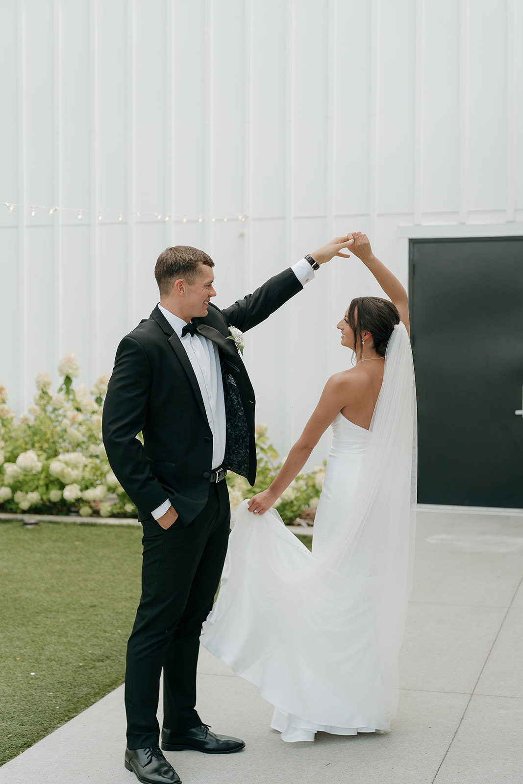 Playful wedding photo of the groom twirling the bride as she lifts her dress, capturing movement and joy outdoors.