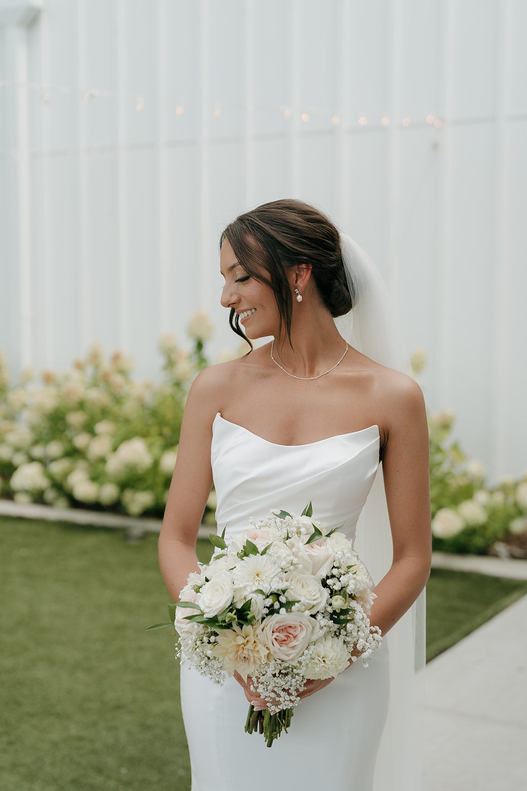 Bridal portrait of the bride holding a white and blush bouquet, looking down and smiling in soft natural light.