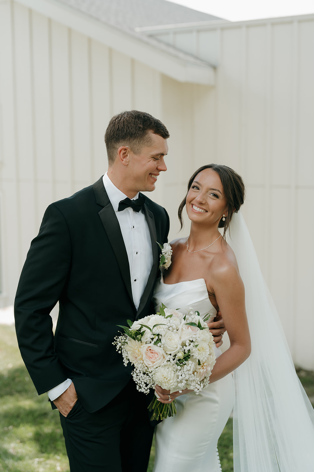 Bride and groom posing together in front of hydrangeas and a white exterior wall at a Des Moines wedding venue, showcasing classic wedding style.