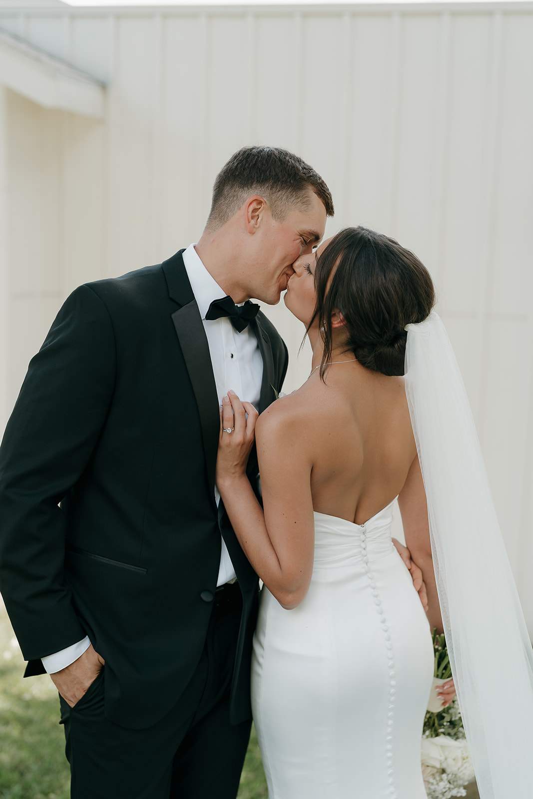 A portrait of the bride and groom kissing and standing close outside a modern Des Moines wedding venue with floral landscaping.