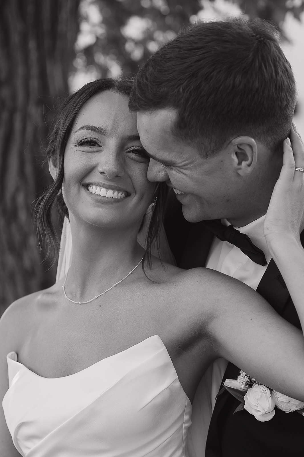 A close up black and white photo of the bride and groom hugging into each other as the bride looks at the camera during bride and groom portraits.
