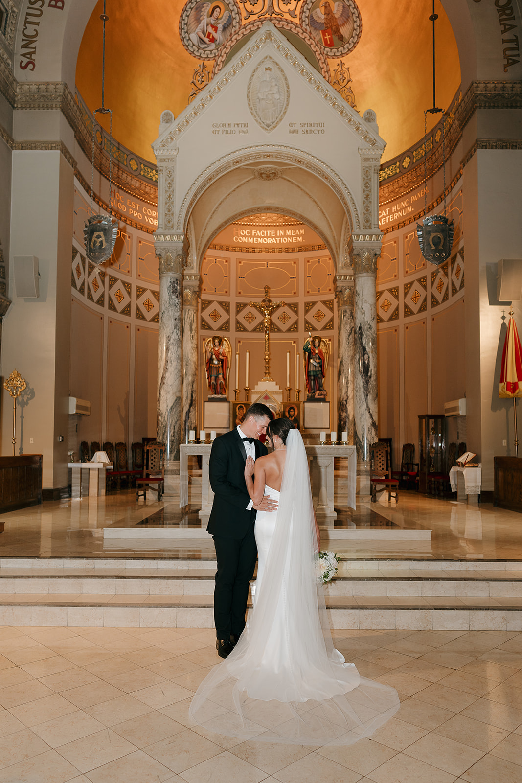 Bride and groom standing together at the altar inside an ornate Catholic church at a Des Moines wedding venue, surrounded by warm golden architecture and marble columns.