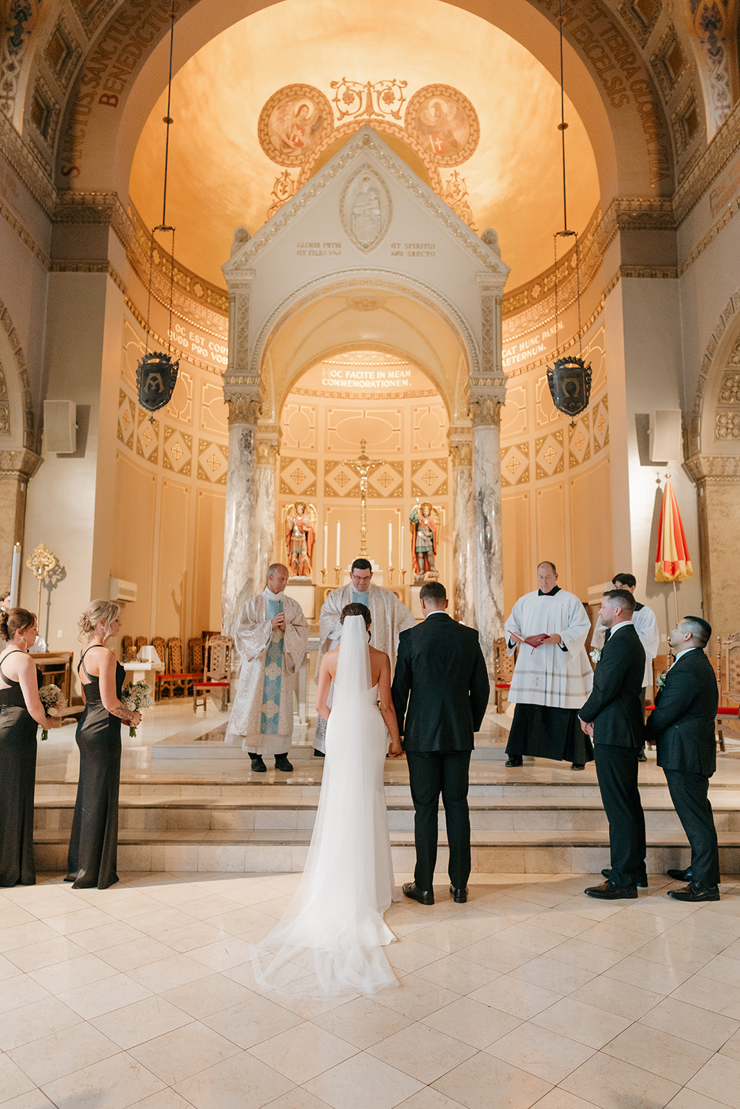 Bride and groom standing together at the altar inside an ornate Catholic church at a Des Moines wedding venue, surrounded by warm golden architecture and marble columns.