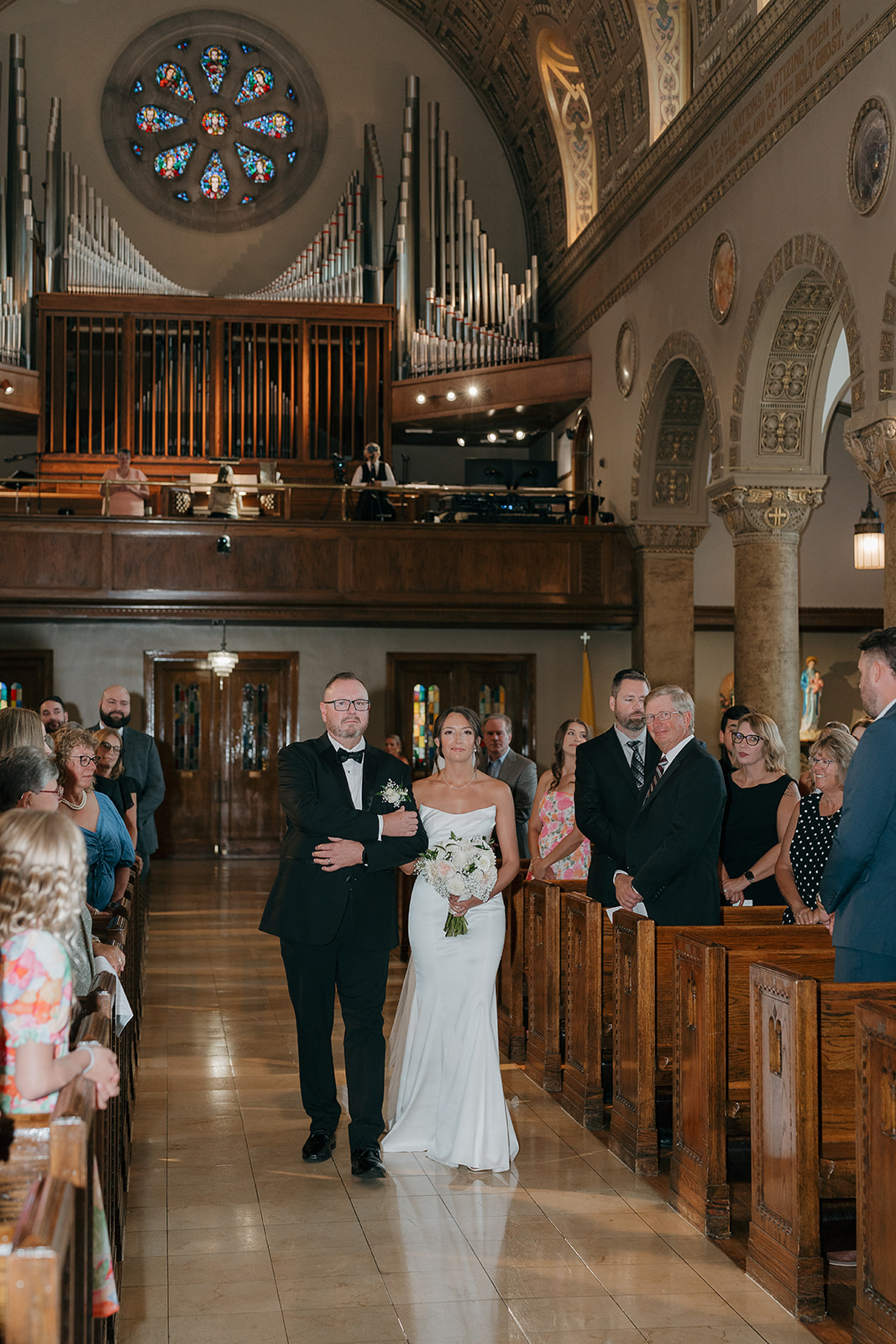 The bride and her dad walking down the aisle inside an ornate Catholic church at a Des Moines wedding venue, surrounded by warm golden architecture and marble columns.