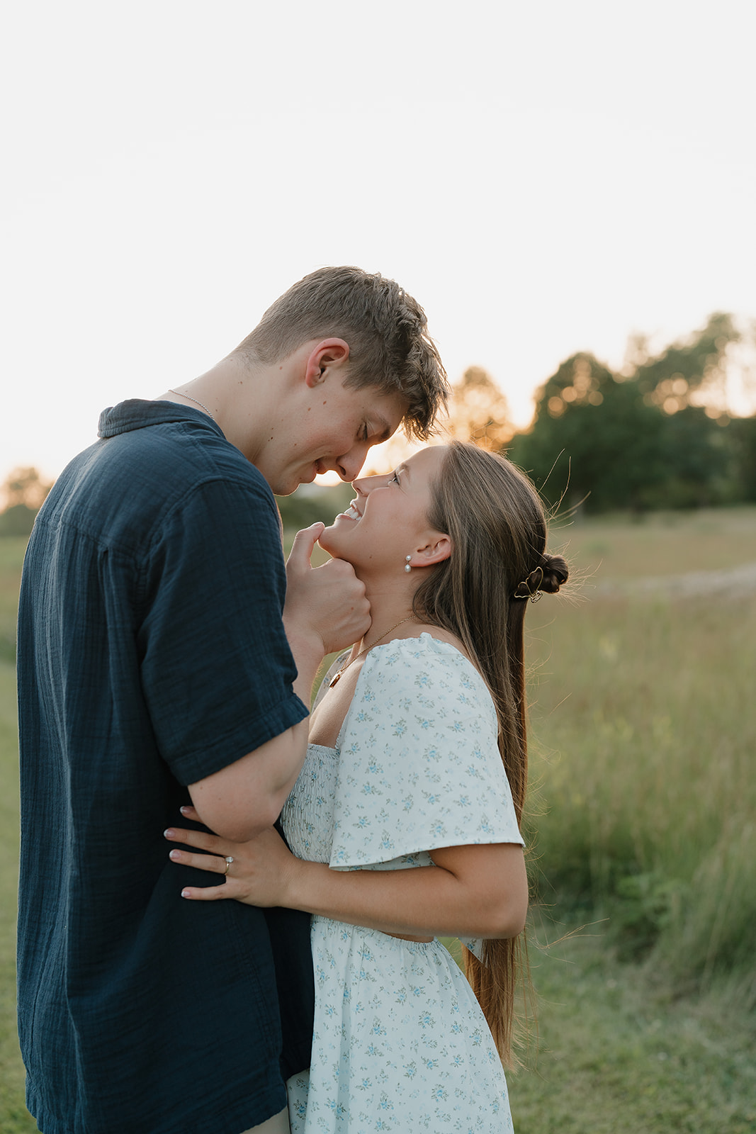 Joyful field engagement session at golden hour, featuring the couple smiling together and standing in a gield during their engagement shoot.
