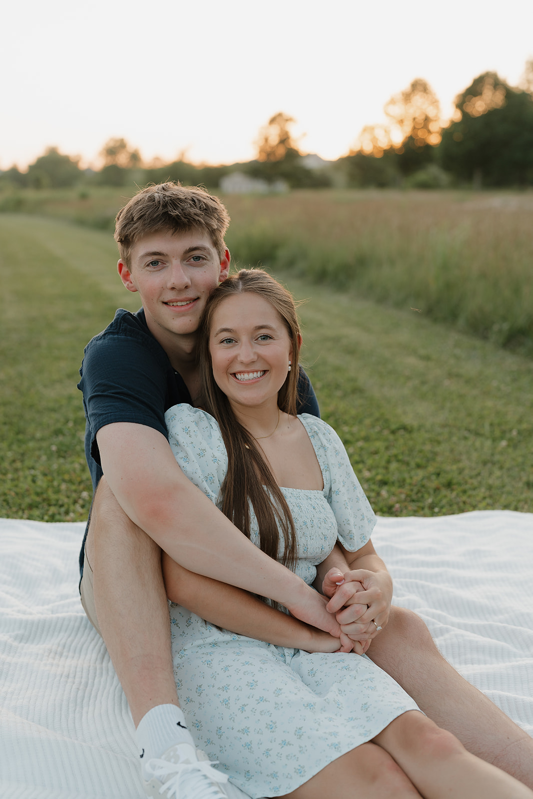 Joyful field engagement session at golden hour, featuring the couple smiling together on a blanket in one of their favorite Unique Engagement Photo Locations.