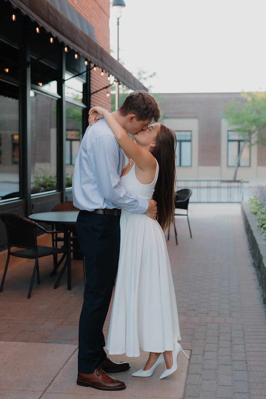 Romantic city engagement portrait of the couple embracing outside a restaurant patio, highlighting charm and character in Unique Engagement Photo Locations downtown.