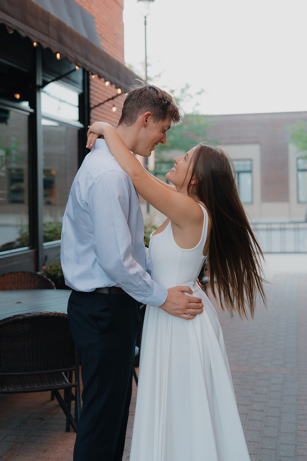 Romantic city engagement portrait of the couple embracing outside a restaurant patio, highlighting charm and character in Unique Engagement Photo Locations downtown.