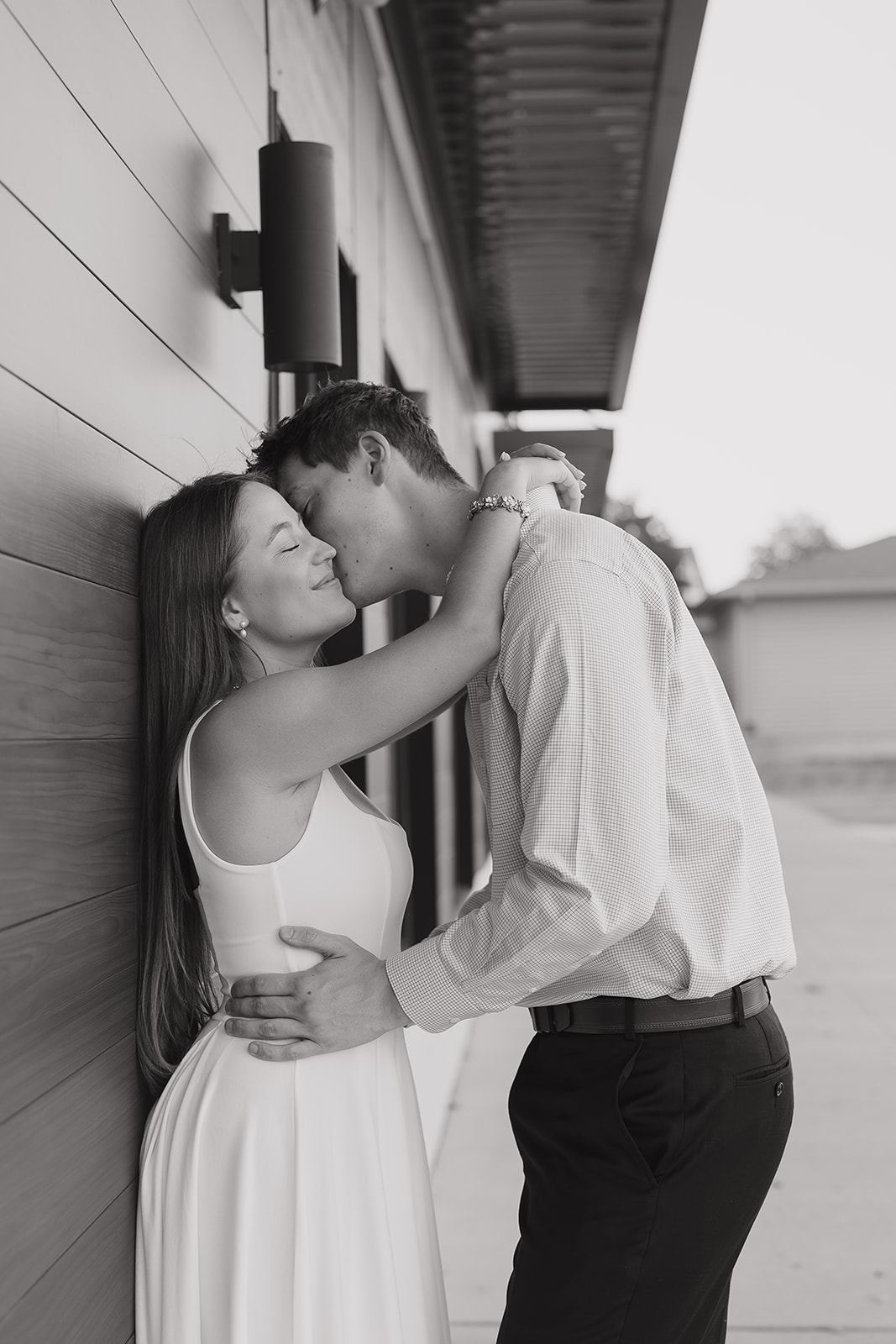 Black and white portrait of engaged couple embracing against a wall, timeless documentary engagement photos style