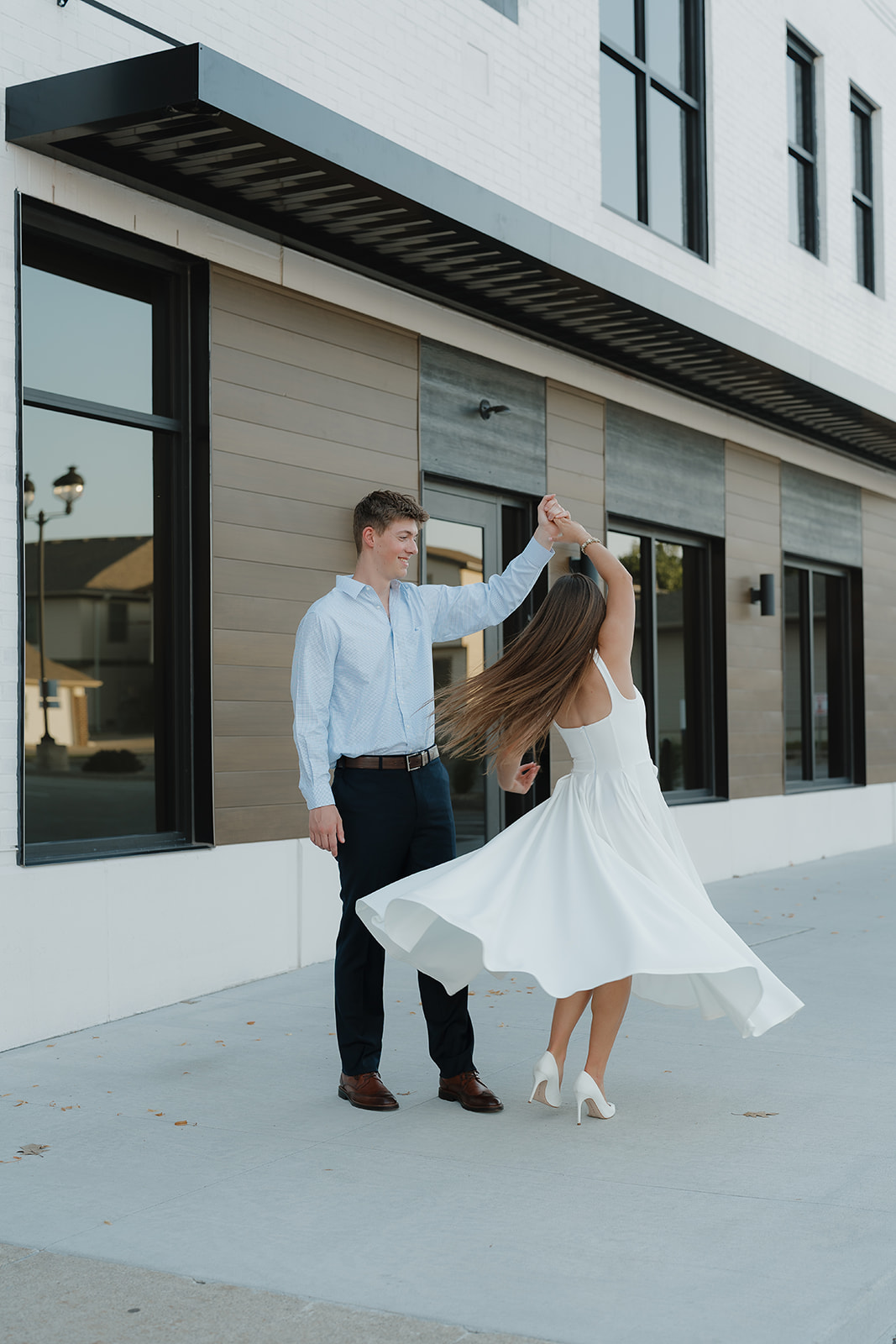 Couple dancing together on a sidewalk outside a modern building, with the bride’s white dress twirling in motion.