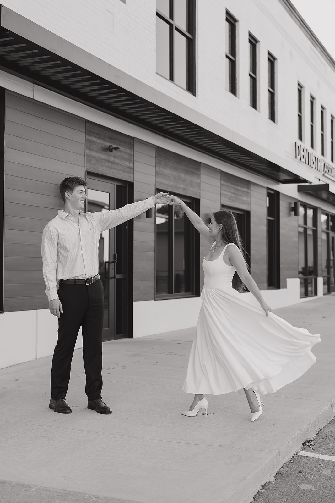Wide black and white photo of bride twirling while holding her soon to be husband's hand downtown.