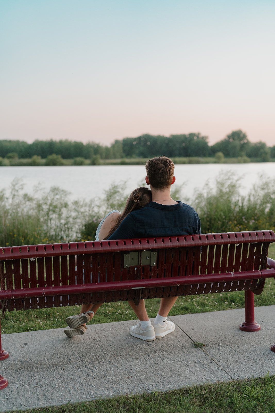 A couple sitting on a park bench while overlooking a lake at sunset during at a unique engagement photo location in Iowa