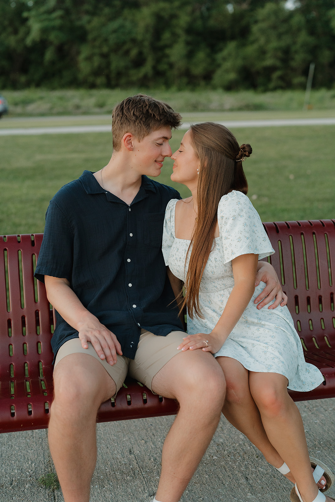 Couple sitting close together on a park bench about to kiss, during their relaxed outdoor engagement session