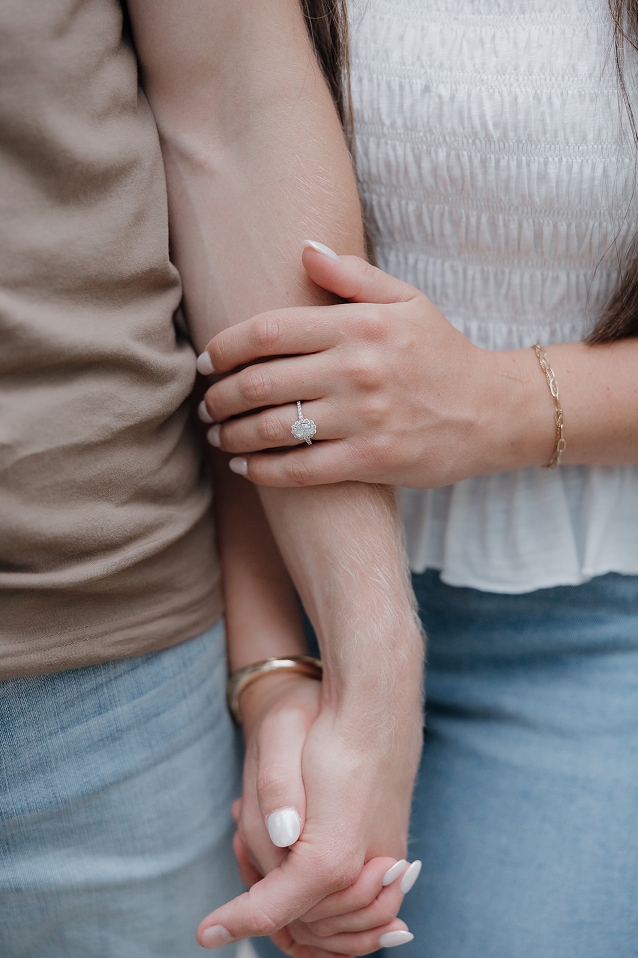 A close-up of an engagement ring with a diamond halo setting as the bride-to-be holds her fiancé's arm