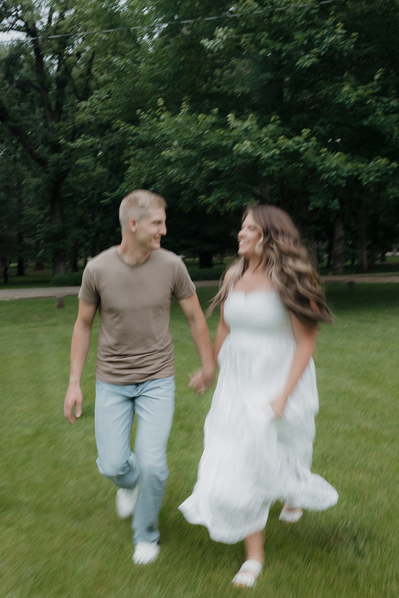 A happy couple running and laughing together across a lush green park lawn