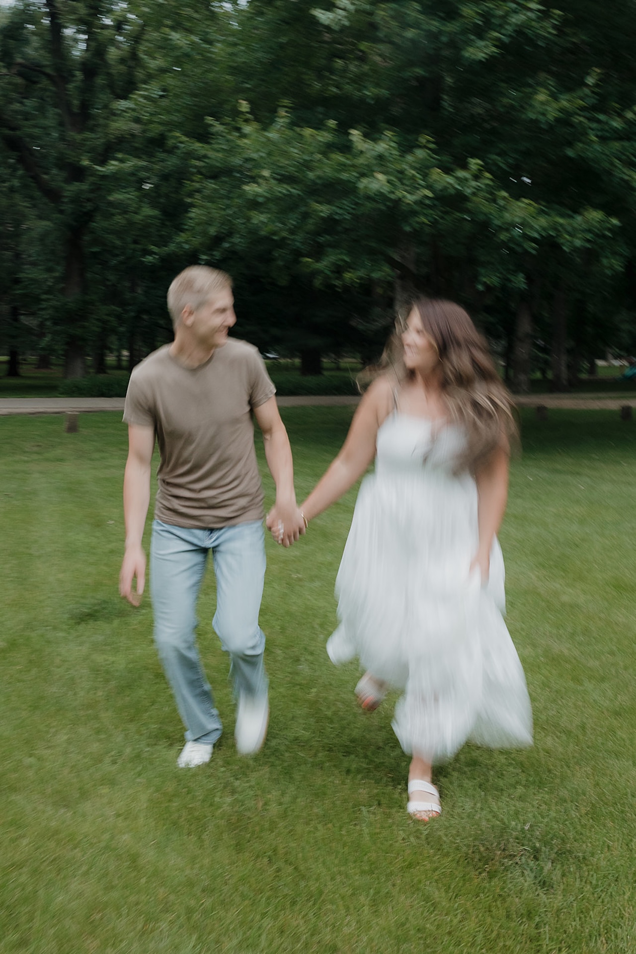 A couple running and laughing hand in hand through a grassy Iowa park, a great reminder of why summer is the best time to take engagement photos