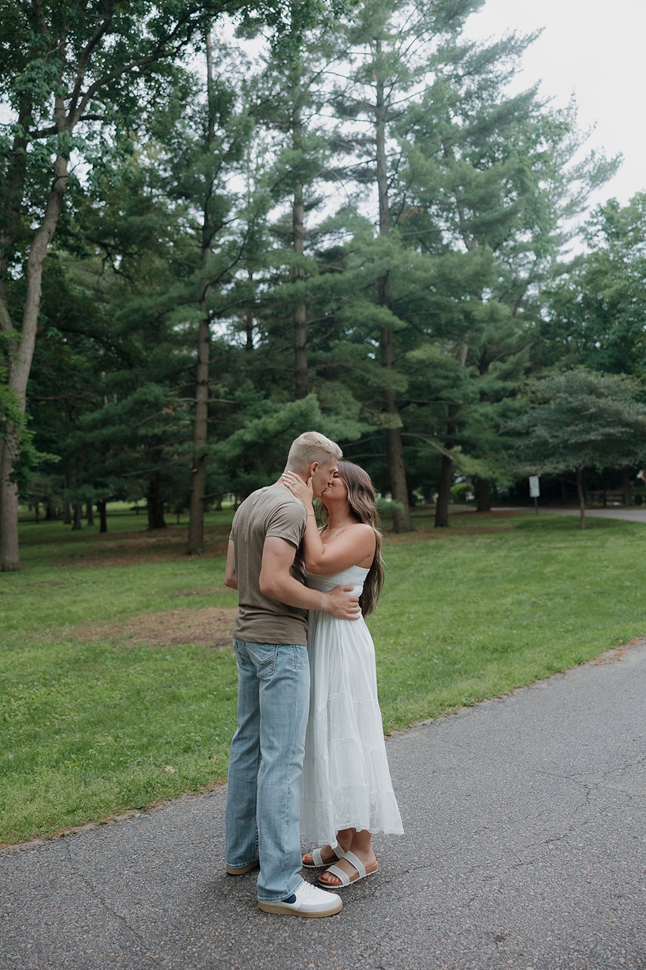 An engaged couple sharing a sweet kiss on a tree-lined park path in Iowa