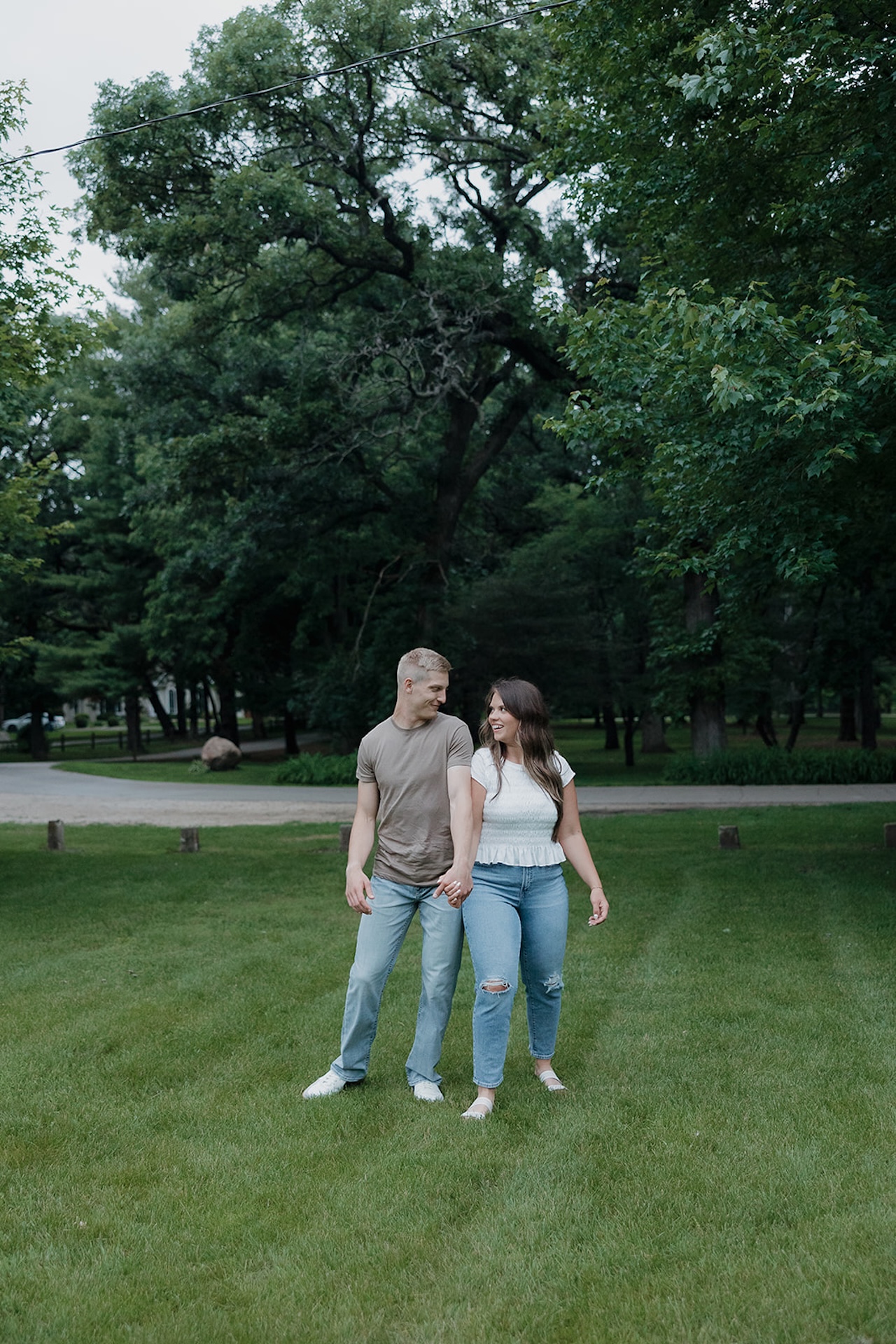An engaged couple holding hands and laughing together in a lush Iowa park — exactly the kind of moment you hope for when to take engagement photos in summer