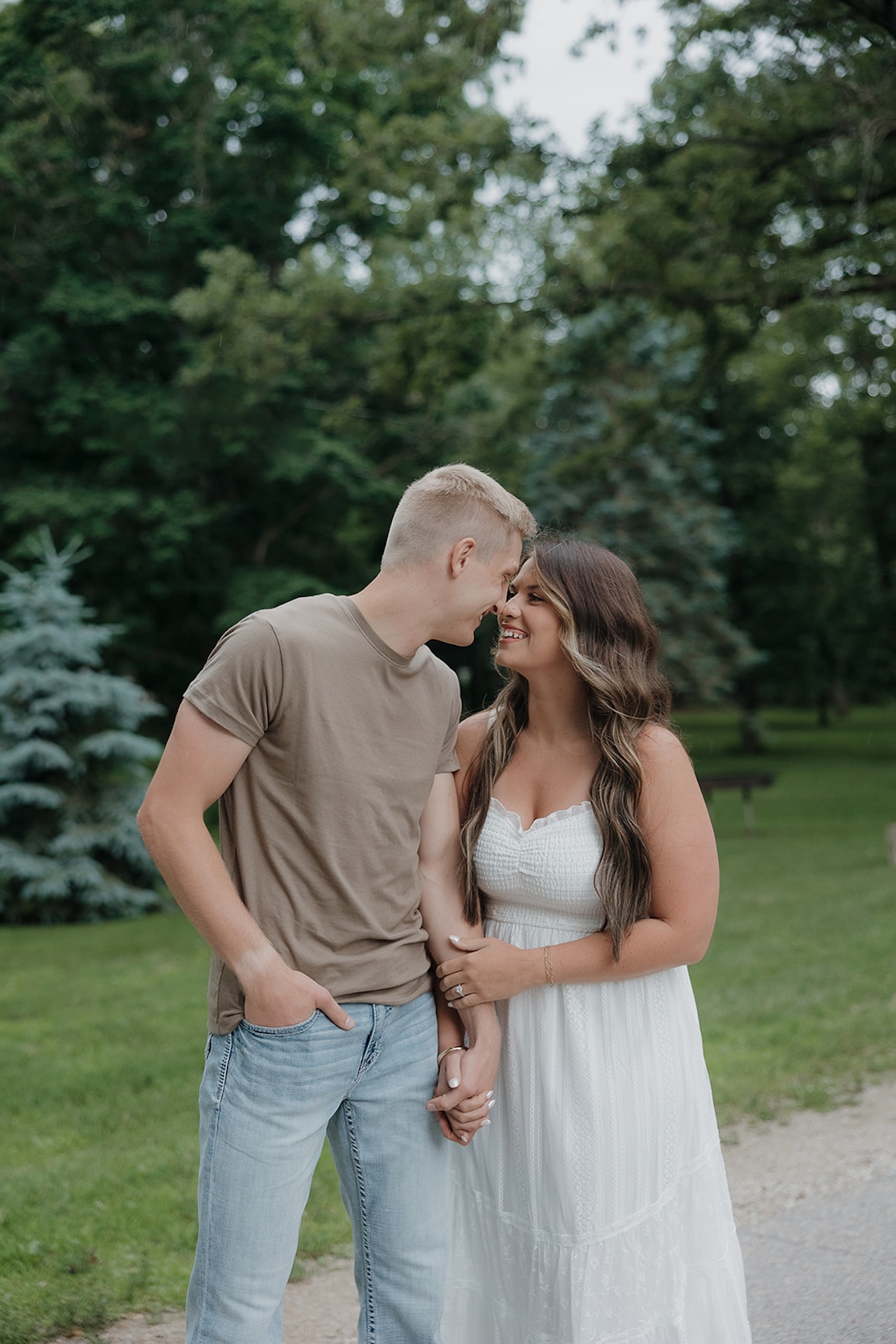 A couple sharing an intimate almost-kiss in a green Iowa park — everything about this moment shows why summer is the best time to take engagement photos