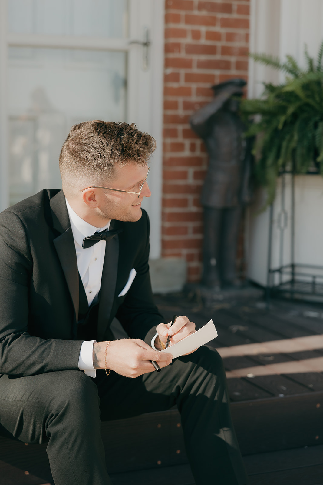 Groom reviewing his vows on the porch of a brick estate
