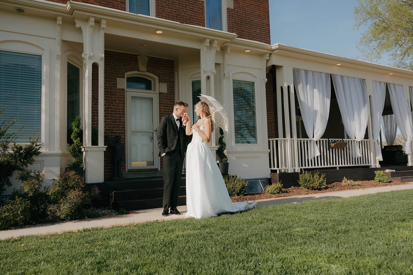 Bride and groom stealing a quiet moment outside their old money wedding venue, parasol in hand, sunlight streaming across the lawn

