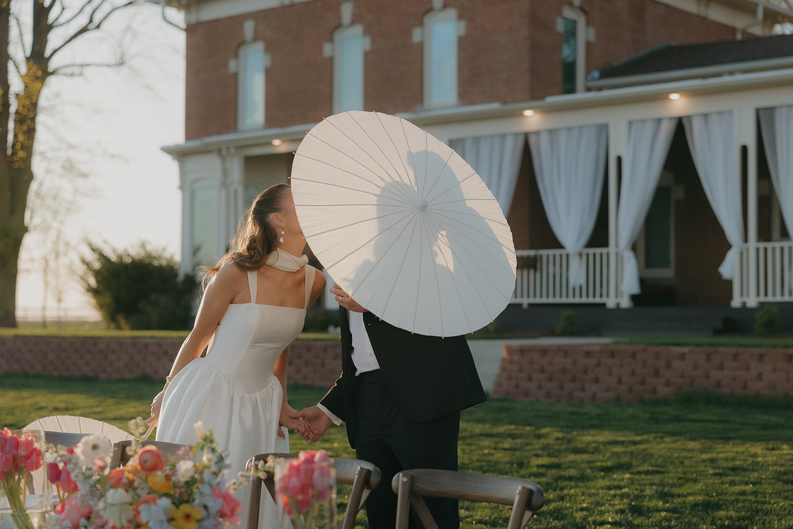 Couple stealing a kiss hidden behind a white parasol in front of their historic old money wedding venue
