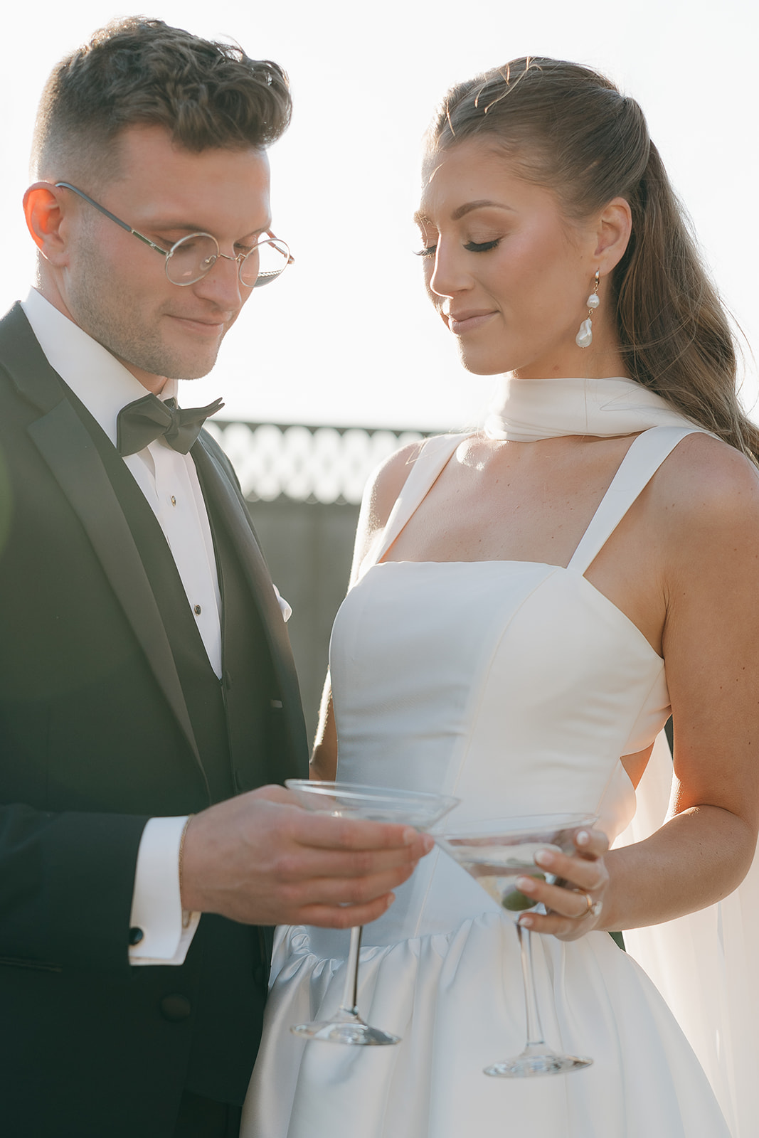 Bride and groom sharing a quiet smile over their martini glasses in warm golden light, an intimate old money wedding portrait
