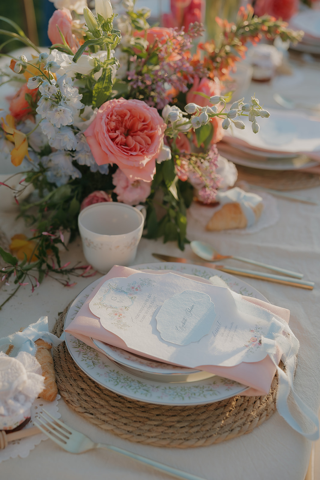 Elegant place setting with a calligraphy menu card, blush napkin, and garden roses trailing across the table

