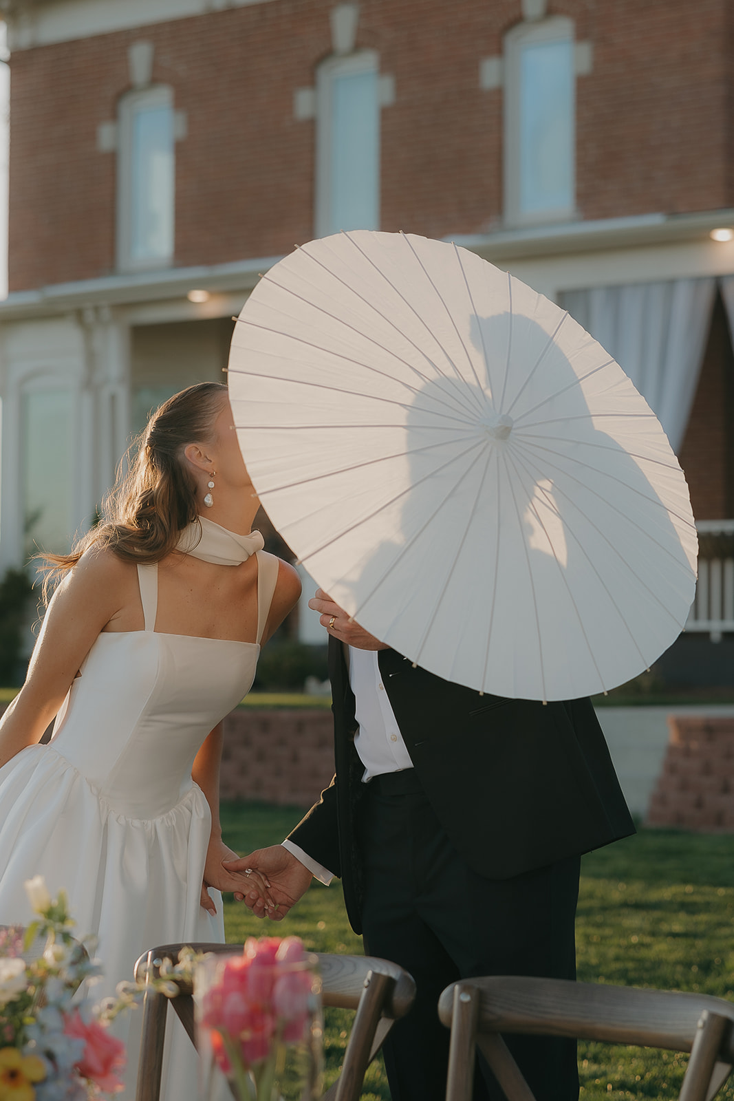 Bride and groom kissing behind a white parasol in front of a historic manor
