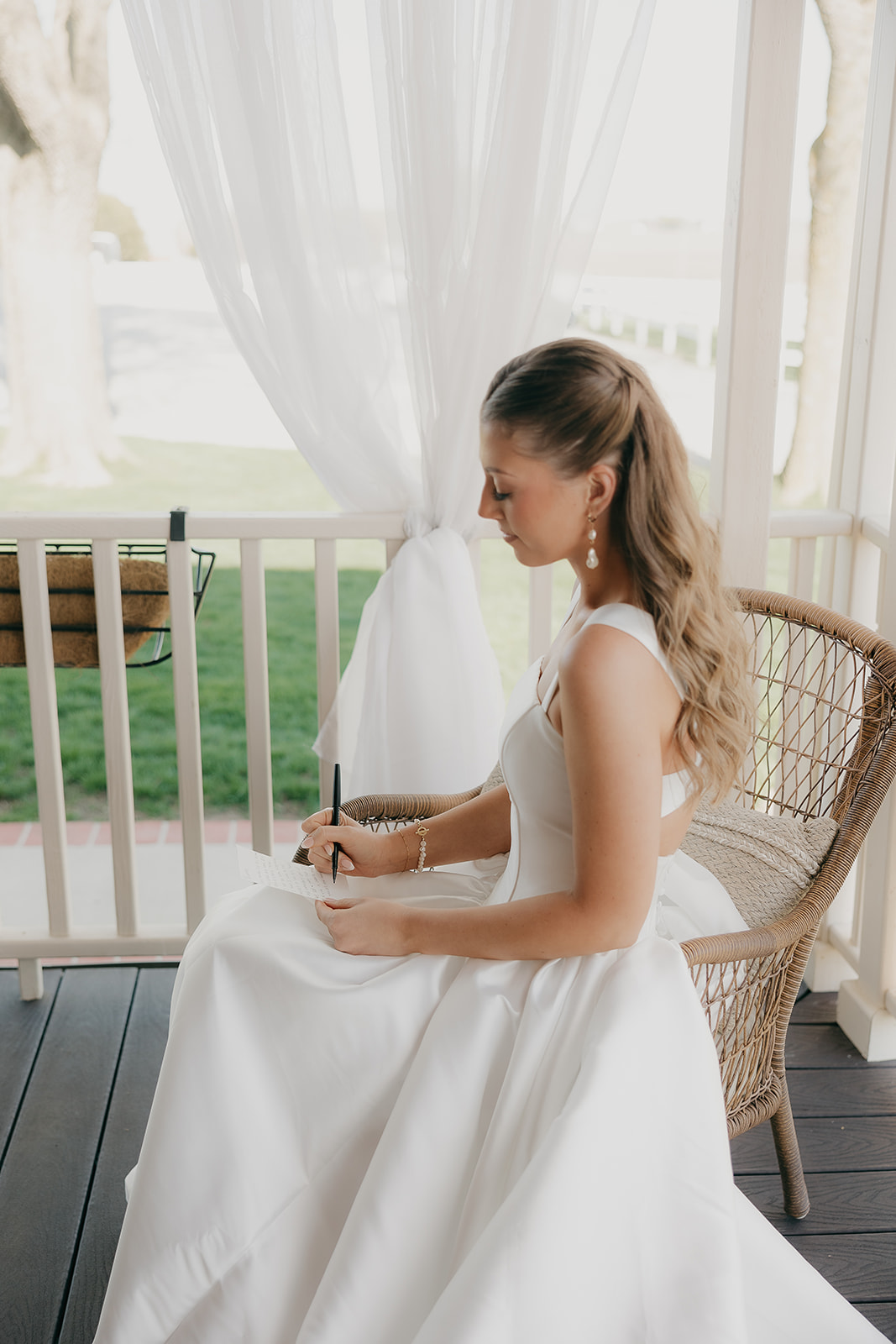 Bride writing her vows while seated on a wicker chair on the porch
