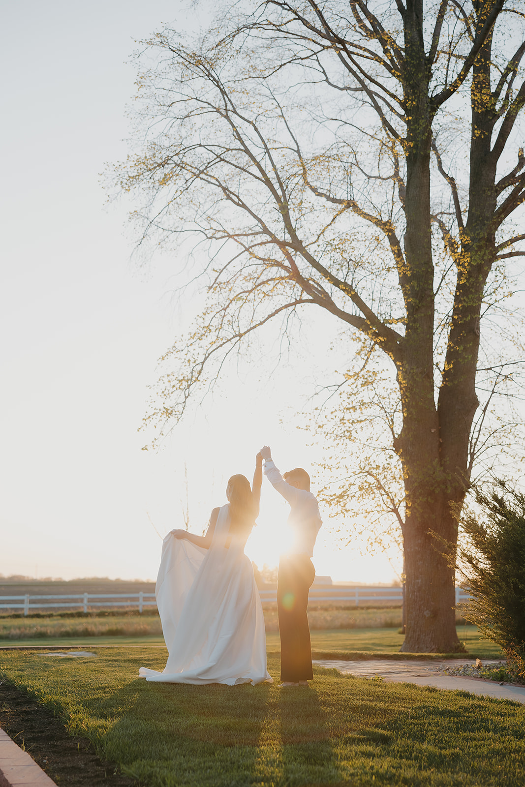 Bride and groom dancing at golden hour under a large tree
