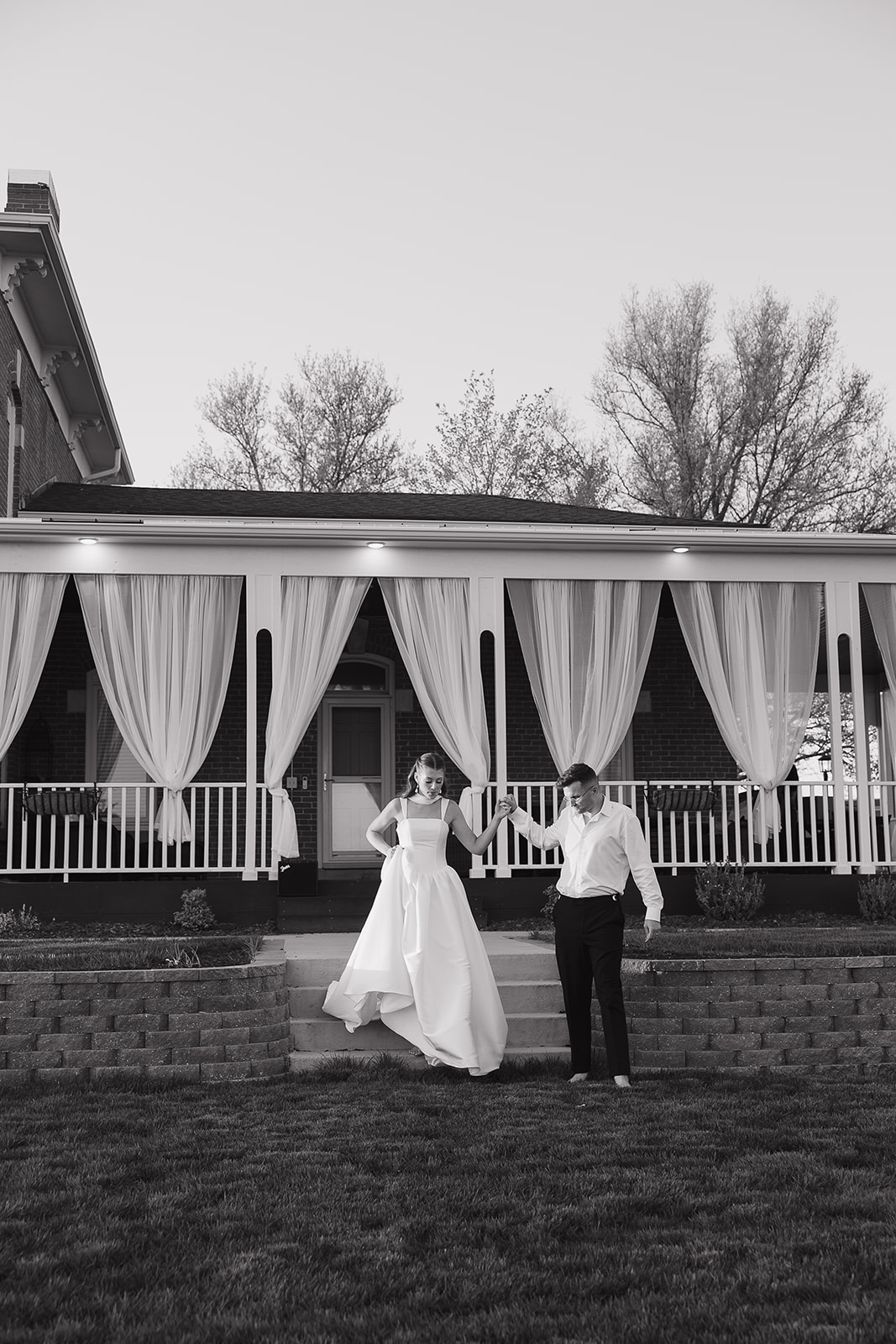 Bride and groom dancing in black and white outside a draped historic manor, the kind of old money wedding venue that feels like it belongs in another era
