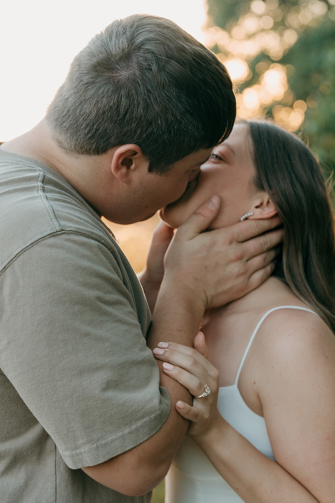 Couples photoshoot ideas captured in a close up of an engaged couple leaning in for a kiss with the man cradling her face and her engagement ring visible between their hands