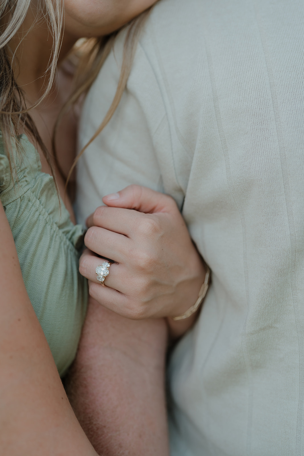 A close-up detail shot of the woman's three-stone diamond engagement ring as she holds her partner's arm during their summer session at Ada Hayden in Iowa
