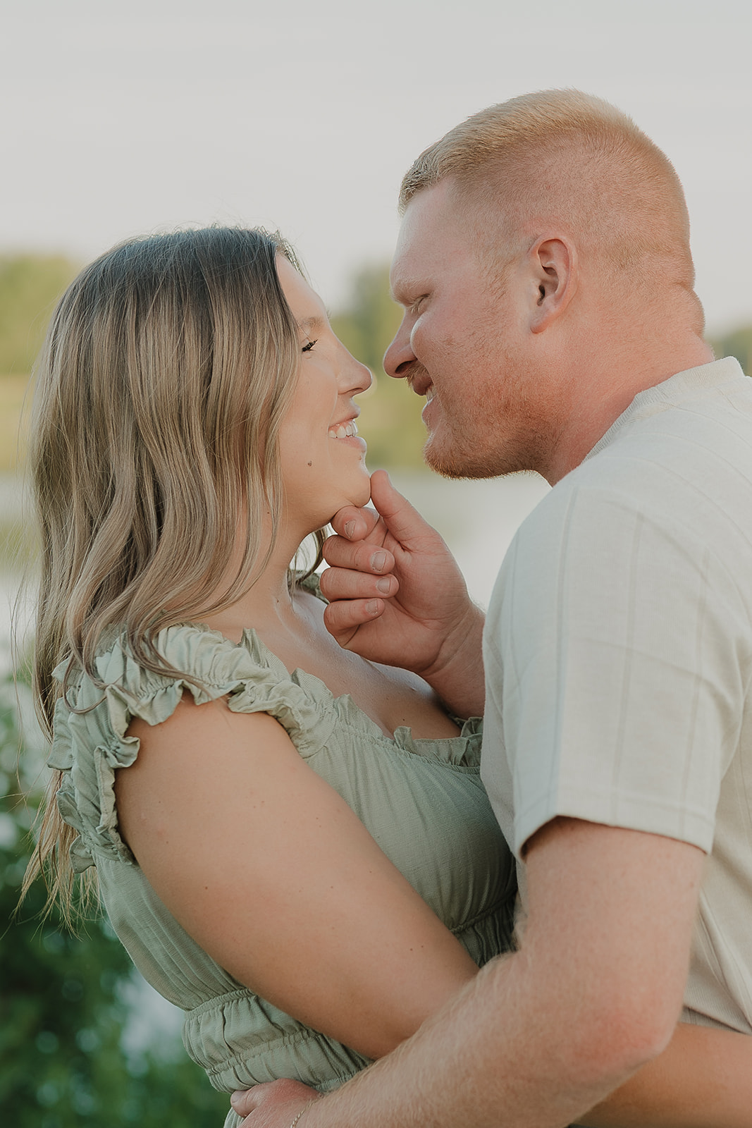 A close-up of the couple nearly touching foreheads and smiling at each other, the woman's sage ruffle dress and her partner's cream tee making ideal summer engagement photo outfits
