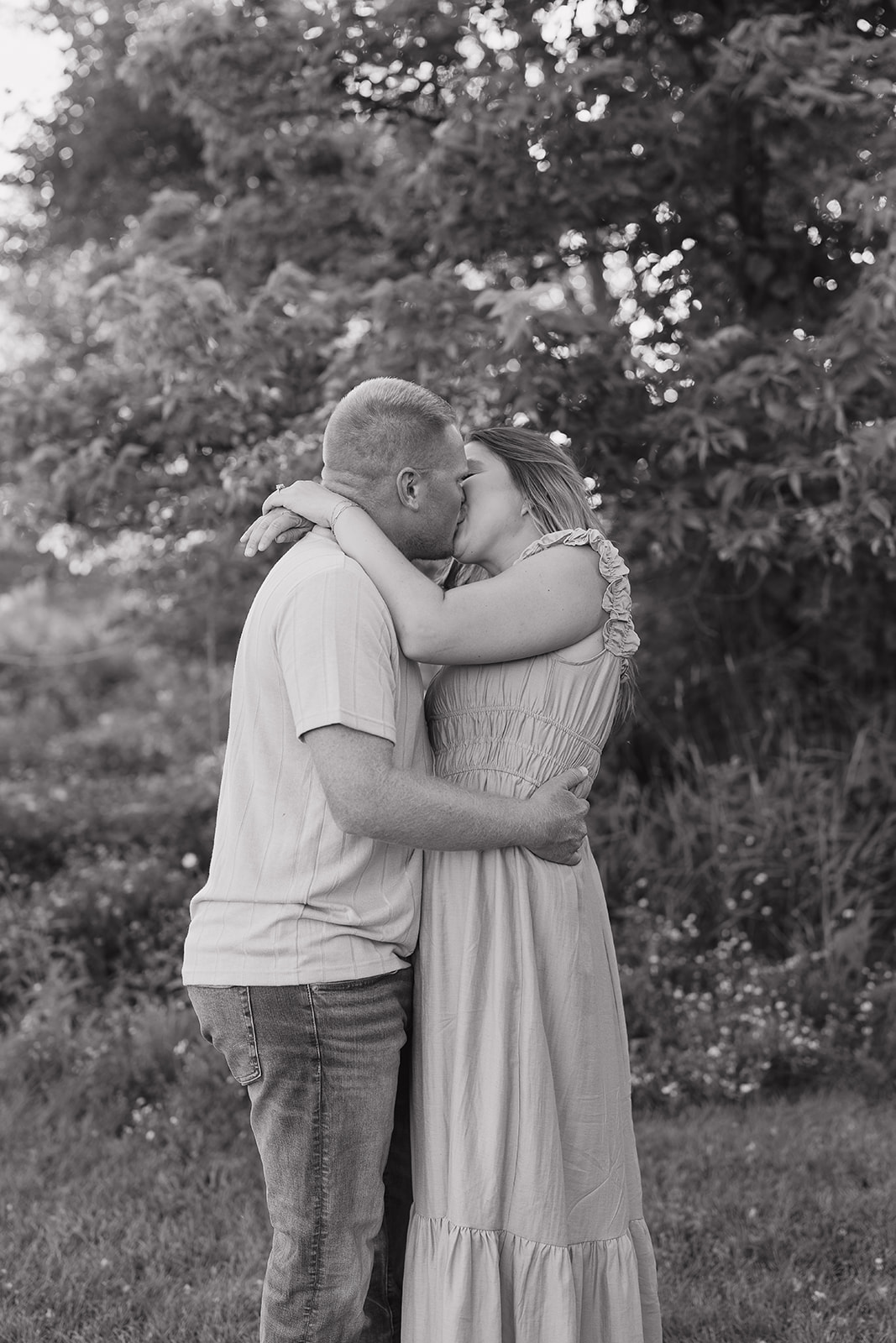 A black and white photo of the couple sharing a deep kiss surrounded by wildflowers and trees during their Iowa engagement session
