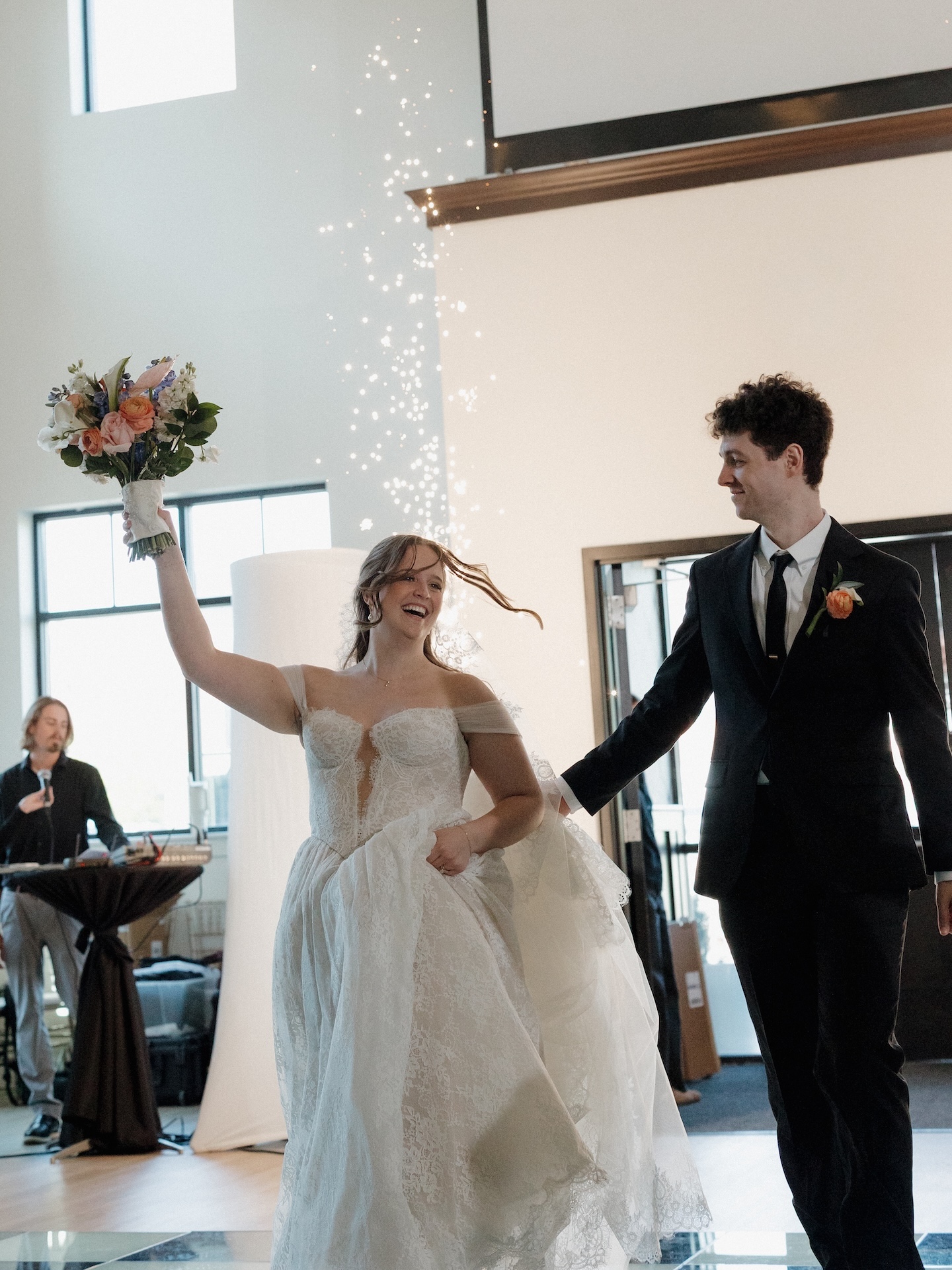 The bride triumphantly raises her bouquet as she and the groom make their grand reception entrance amid sparkling effects at The District

