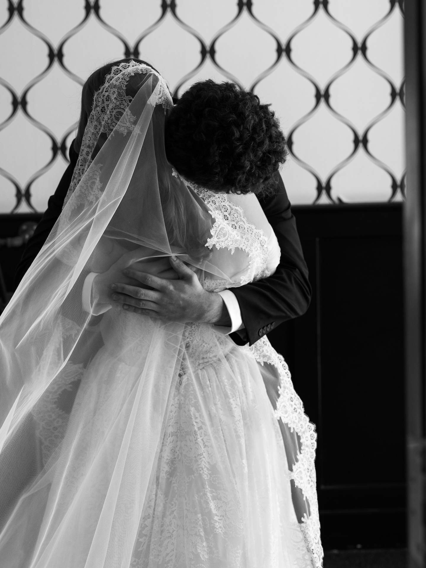 A black and white photo of the bride and groom embracing in an intimate first look, the groom's hand resting on the bride's back
