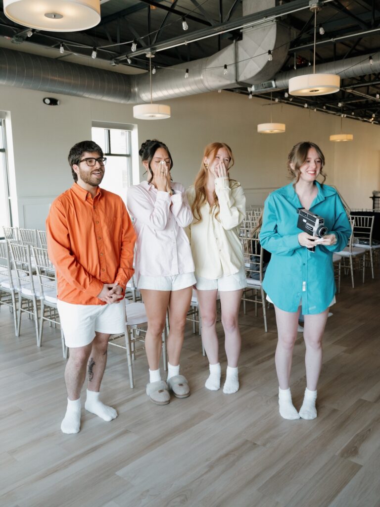 Bridesmaids and a groomsman in colorful button-down shirts react with happy tears and laughter as they see the bride for the first time at The District
