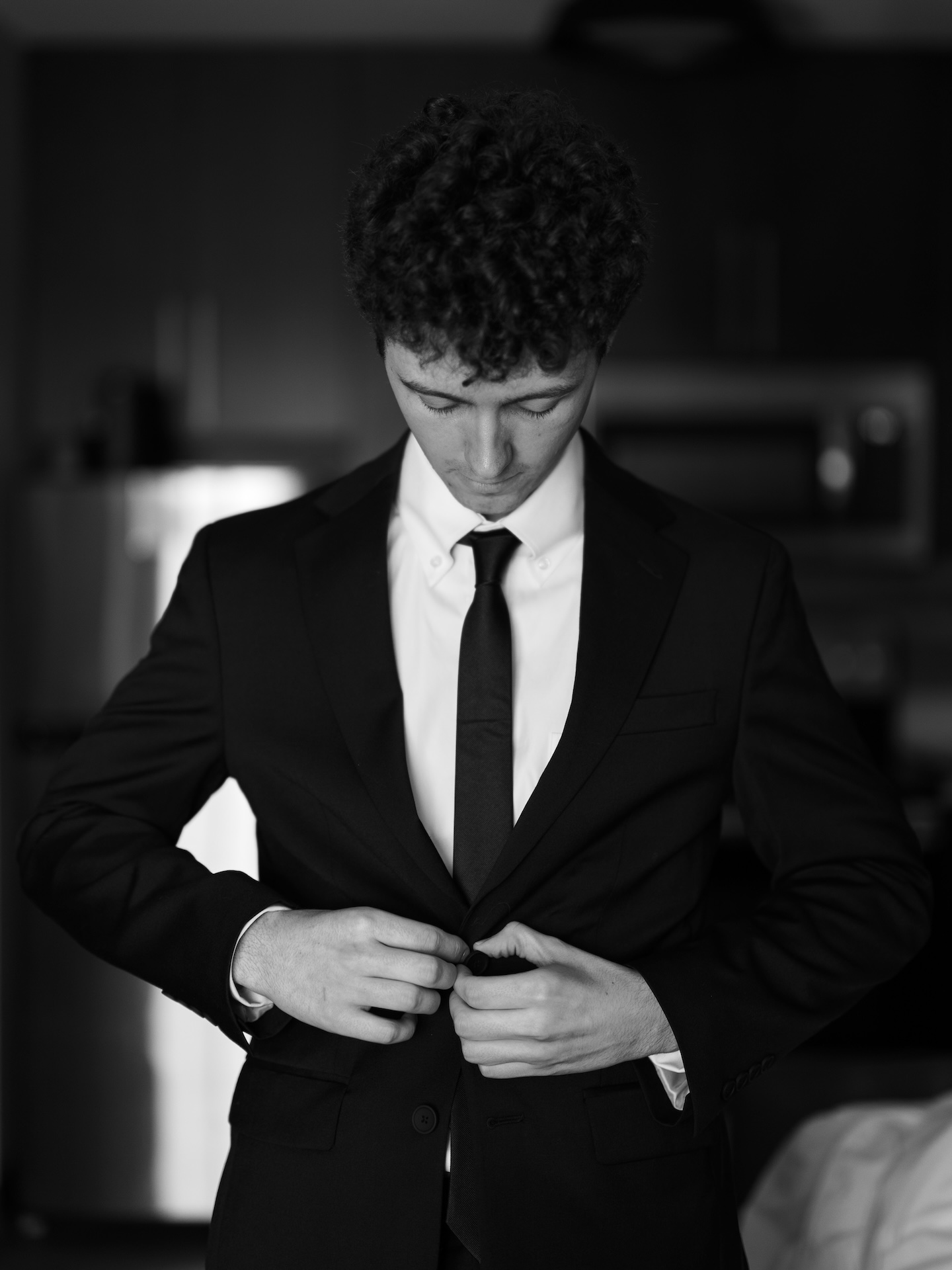 A black and white portrait of the groom buttoning his suit jacket while getting ready on his wedding morning
