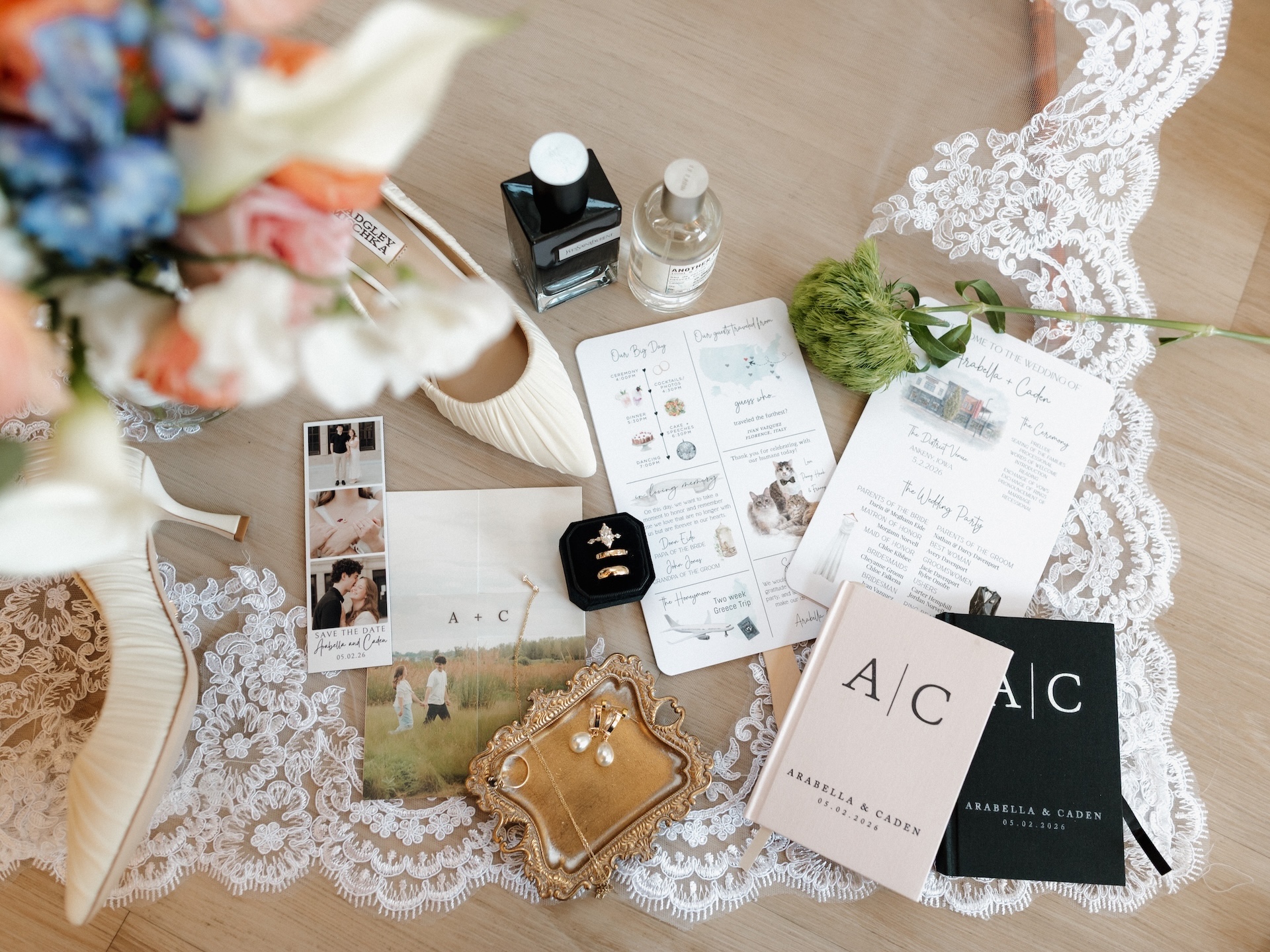 A styled wedding flat lay featuring the bride's heels, rings, pearl earrings, perfume bottles, save the date, programs, and vow books for Arabella & Caden
