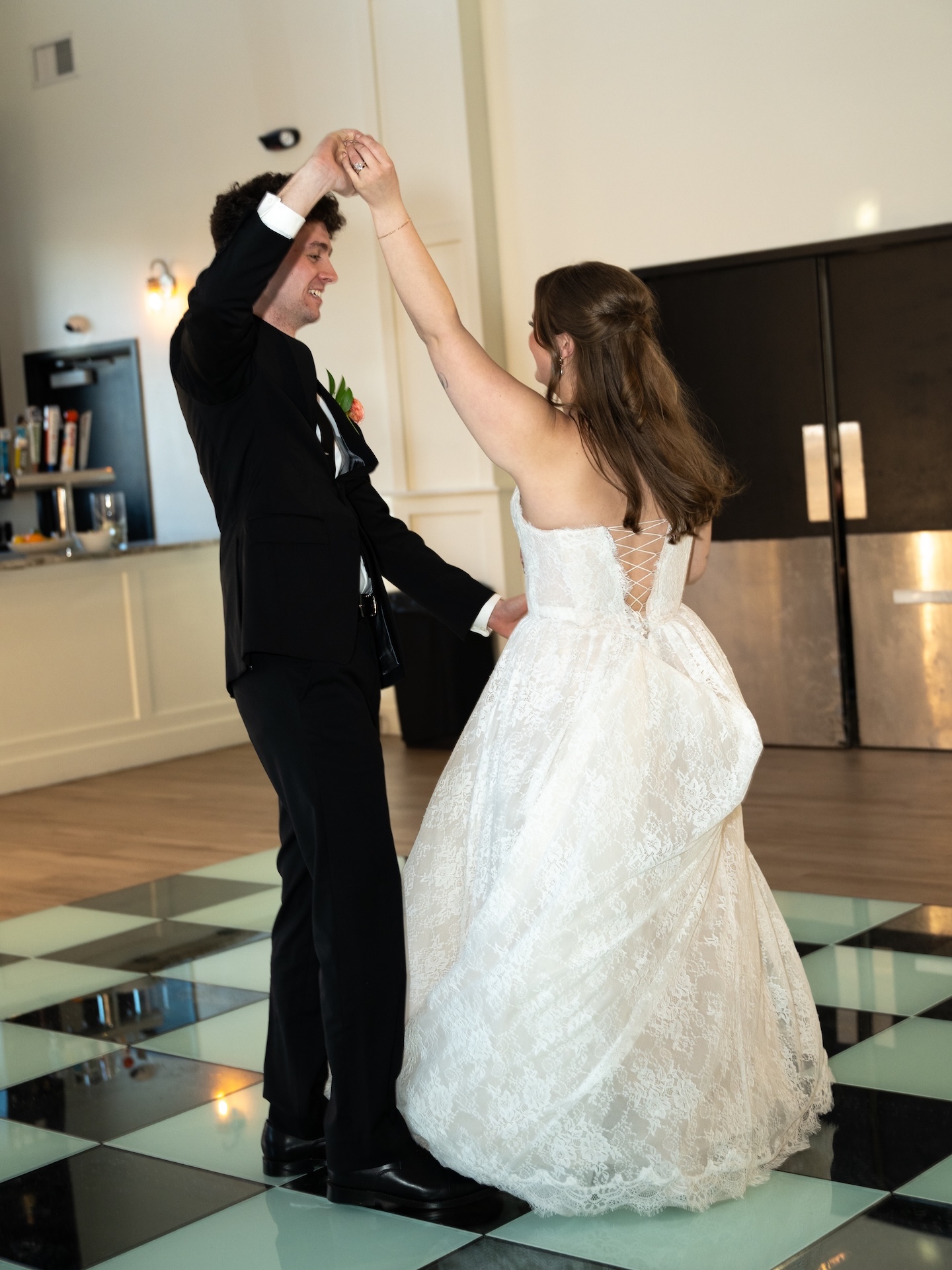 The groom twirls the bride on the black and white checkered dance floor during their first dance at the summer wedding reception
