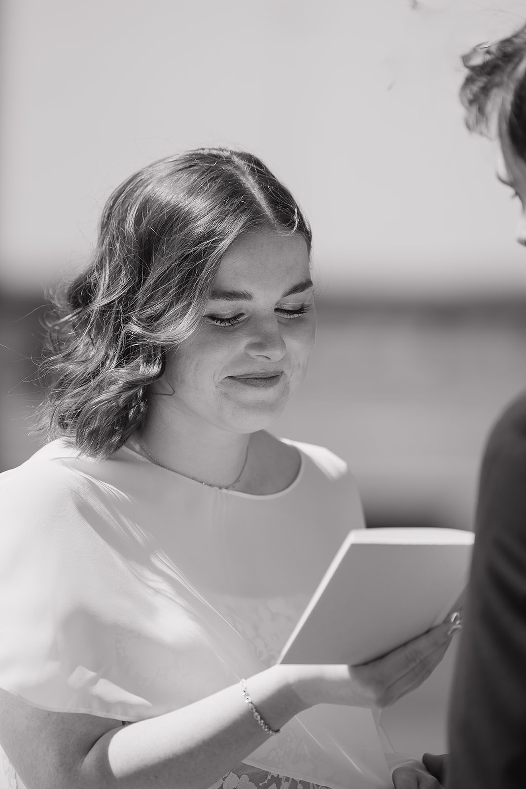 Bride reading her vows with a soft smile during a sun-drenched outdoor wedding ceremony