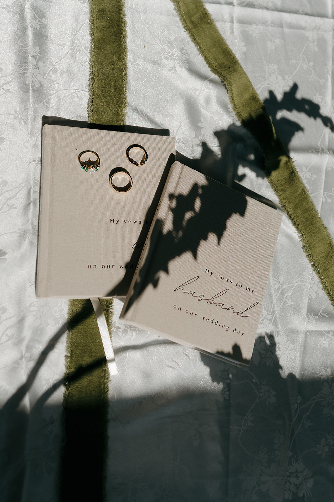 Wedding rings and vow books styled with dramatic shadow play on white linen in a moody detail flat lay
