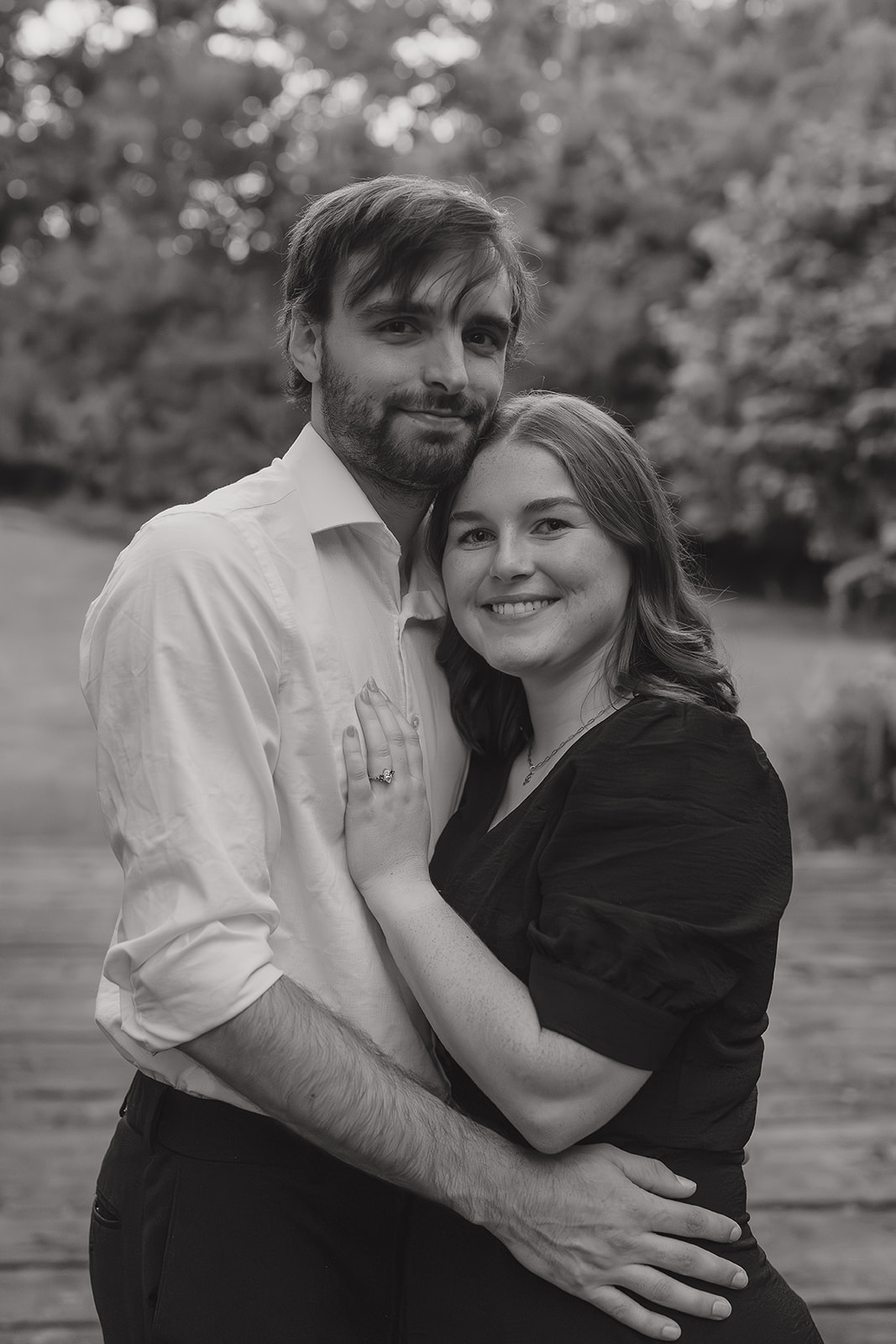 Fall engagement photos of a newly engaged couple embracing and smiling at the camera in a black and white portrait outdoors

