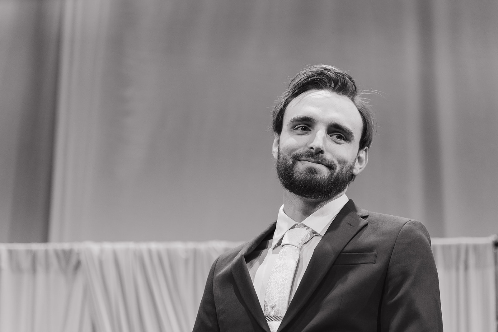 Black and white portrait of a smiling groom waiting at the altar during the wedding ceremony